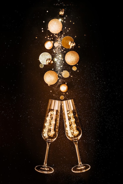 Weihnachtskomposition. Gläser mit Champagnerwein aus goldenen festlichen Dekorationen auf schwarzem Hintergrund mit Glitzer. Das Konzept einer Party und eines festlichen Festes.