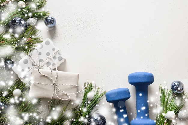 Weihnachtskomposition mit blauen Hanteln, Geschenk und schneebedeckten Tannenzweigen