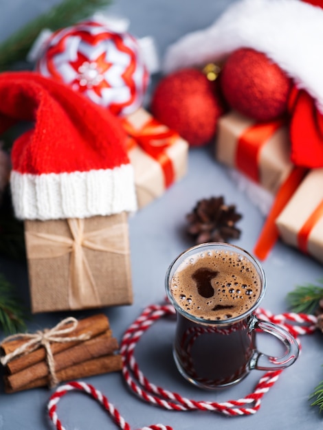 Weihnachtskomposition mit Geschenkboxen in der Weihnachtsmütze und einem Glas Kaffee