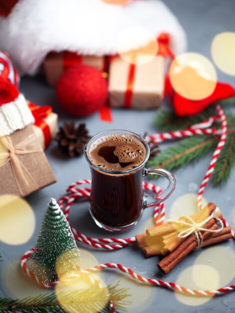 Weihnachtskomposition mit Geschenkboxen in der Weihnachtsmütze und einem Glas Kaffee