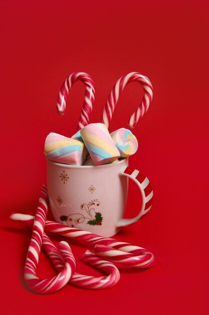 Weihnachtskomposition mit heißem Schokoladengetränk, dekoriert mit Marshmallows und Zuckerstangen einzeln auf rotem Hintergrund mit Kopierraum für Werbung