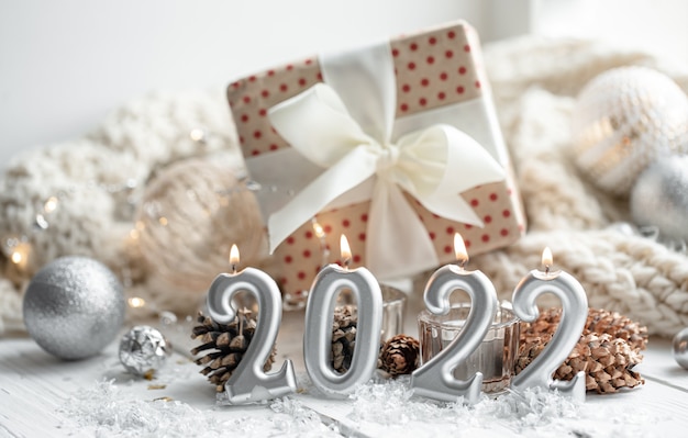 Weihnachtskomposition mit Kerzen in Form der Zahlen 2022, einer Geschenkbox und festlichen Dekordetails auf unscharfem Hintergrund.