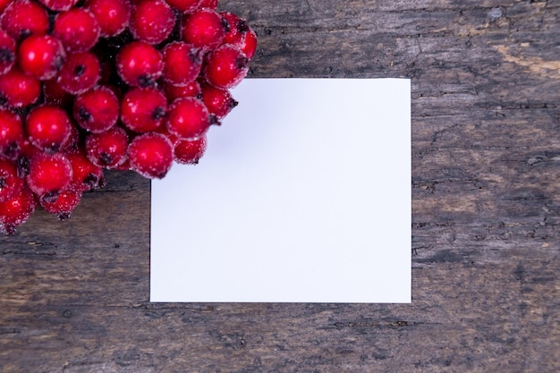 Weihnachtskomposition. Papierrohling mit Rowan Weißdornzweig mit Beeren auf einem hölzernen Hintergrund