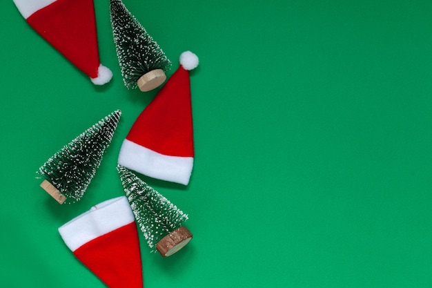 Weihnachtskomposition. Weihnachtsbäume und Weihnachtsmützen auf grünem Hintergrund. Flache Lage, Ansicht von oben, Kopienraum