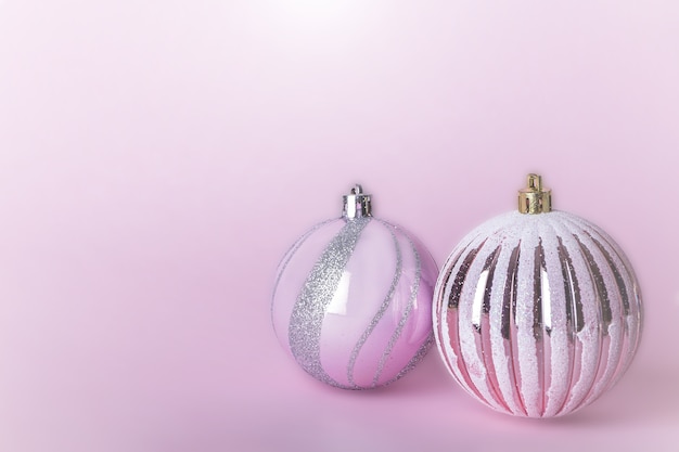 Weihnachtskomposition. Zwei weihnachtliche rosa Kugeln, glänzende Kugeln, die auf Pastellhintergrund hängen