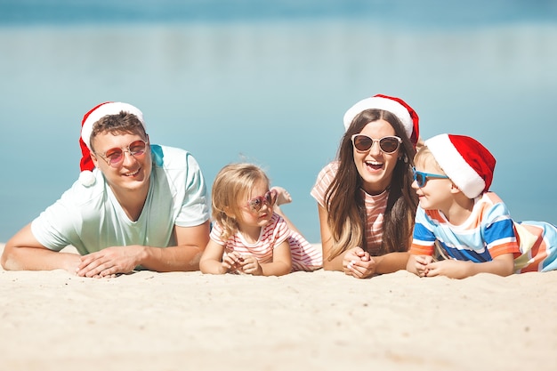 Weihnachtskonzept. Familie, die Weihnachtsmützen am Strand trägt