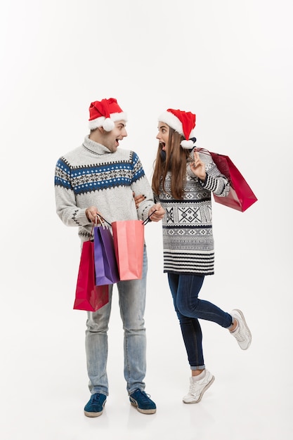 Weihnachtskonzept - in voller Länge Junge attraktive Paare, die Einkaufstaschen lokalisiert auf weißem grauem Hintergrund halten.