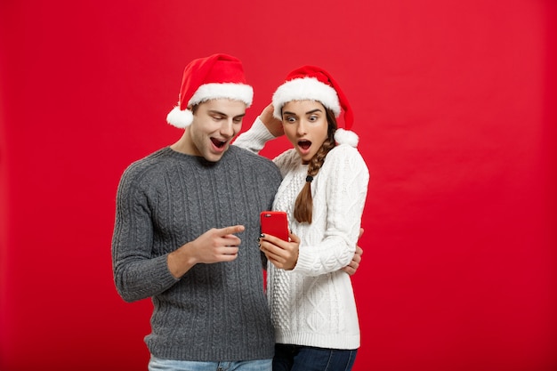 Weihnachtskonzept - Junges hübsches und schönes Paar genießt das Überprüfen auf dem Mobiltelefon am Weihnachtstag.