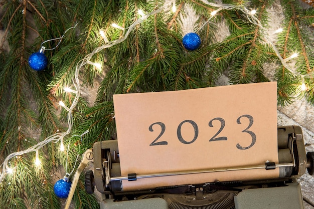 Weihnachtskonzept-Schreibmaschine mit Text 2023 Fichtenzweigen und Girlande