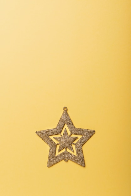Foto weihnachtskonzept. weihnachtskarte mit goldenem stern auf der gelben oberfläche. ansicht von oben nach unten mit kopierraum