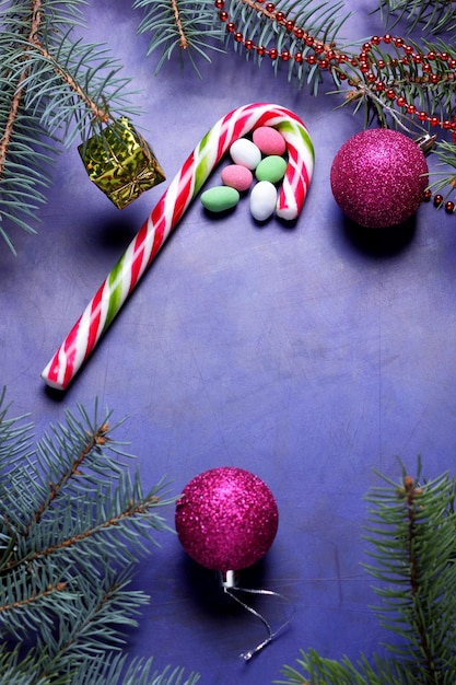 Weihnachtskonzept Weihnachtsspielzeug Zuckerstange Weihnachtsbaum Zweige auf lila Hintergrund Nahaufnahme