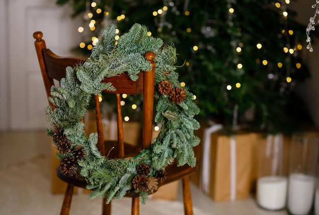 Weihnachtskranz auf einem Stuhl zu Hause auf dem Hintergrund eines grünen Weihnachtsbaums Geschichten des neuen Jahres