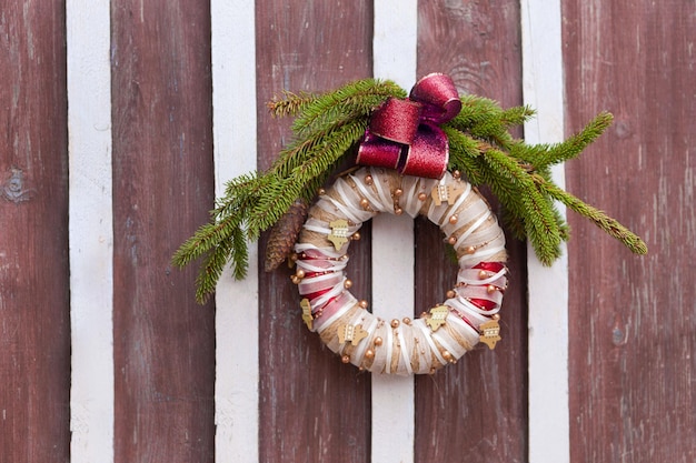 Weihnachtskranz auf Holztür im Ring befestigt und zur Dekoration mit roter Schleife verwendet