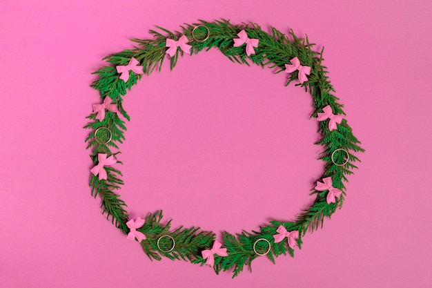 Weihnachtskranz aus Tannenzweigen und Dekorationen auf rosafarbenem Hintergrund. Flache Lage, Ansicht von oben, Kopienraum. festliche Komposition