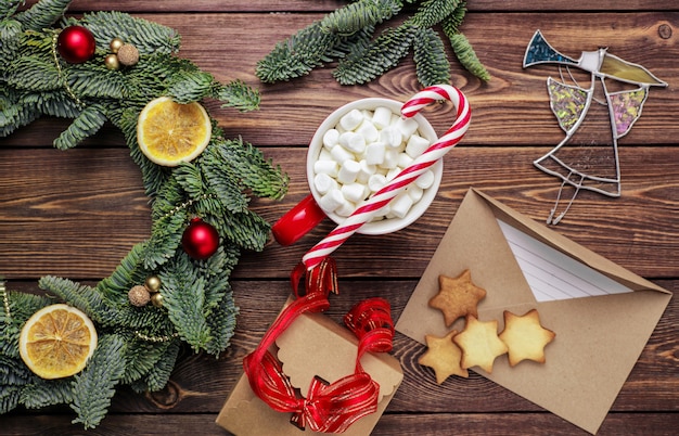 Weihnachtskranz Geschenk Kaffeetasse mit Marshmallows Umschlag und hausgemachte Kekse auf dem Holztisch