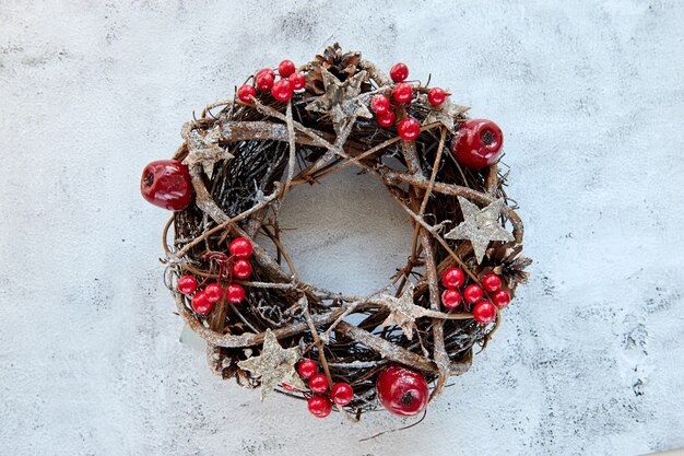 Weihnachtskranz Hergestellt aus Zweigen, die mit goldenen Holzsternen und roten Beerenblasen auf Zementhintergrund verziert werden