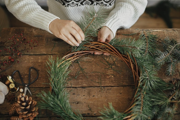 Weihnachtskranz machen Draufsicht Frau mit Tannenzweigen auf rustikalem Hintergrund Winter-Workshop