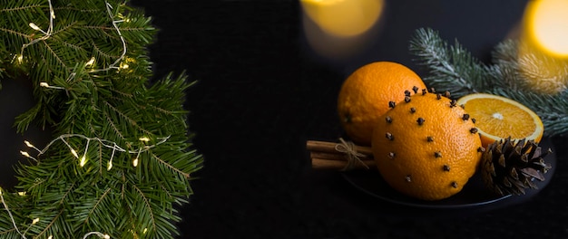 Weihnachtskranz oder Ring und Orangen Gewürznelken und Zimt auf der schwarzen Platte auf dem schwarzen Hintergrund Banner Closeup