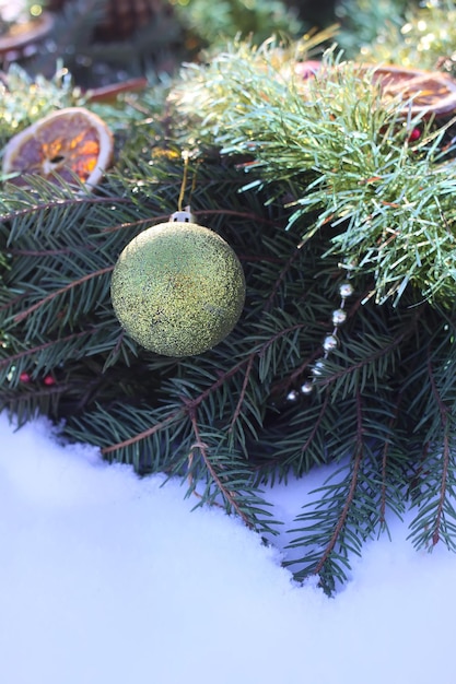 Weihnachtskranz verziert mit trockenen Orangenscheiben und bunten Kugeln auf weißem Schneehintergrund.