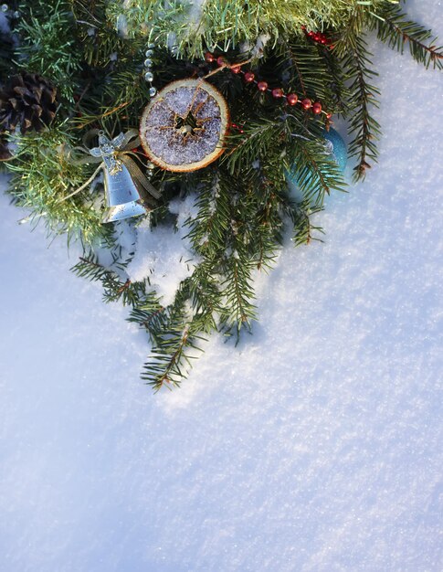 Weihnachtskranz verziert mit trockenen Orangenscheiben und bunten Kugeln auf weißem Schneehintergrund.