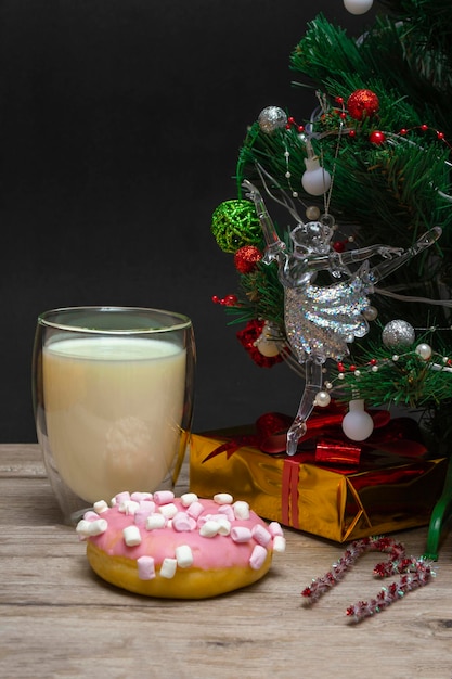 Weihnachtskrapfen und Milch für den Weihnachtsmann. Ein großes Glas mit Milch- und Feiertagsdekorationen. Vertikales Foto eines Weihnachtsgetränks auf einem hölzernen Hintergrund. Nahaufnahme