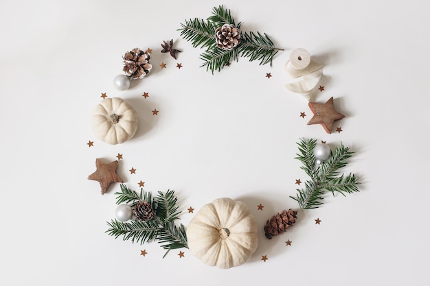 Weihnachtskreis Blumenkomposition Kranz aus Tannenzweigen Tannenzapfen Konfetti Holzsterne weiße Pumkins auf weißem Hintergrund Winteradvent Design und Dekoration Flache Ansicht von oben