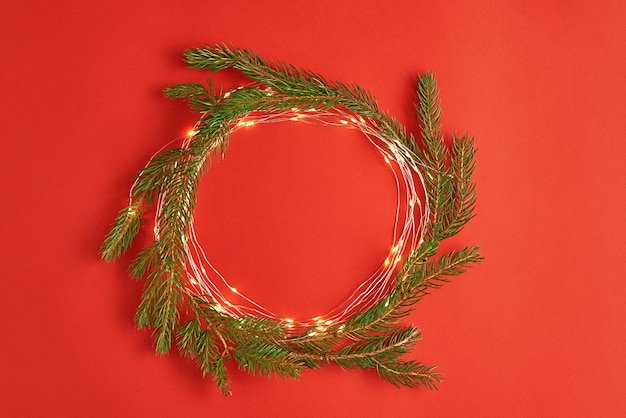 Weihnachtskreiskomposition mit Tannenzweigen und Beleuchtungsgirlande auf rotem Hintergrund