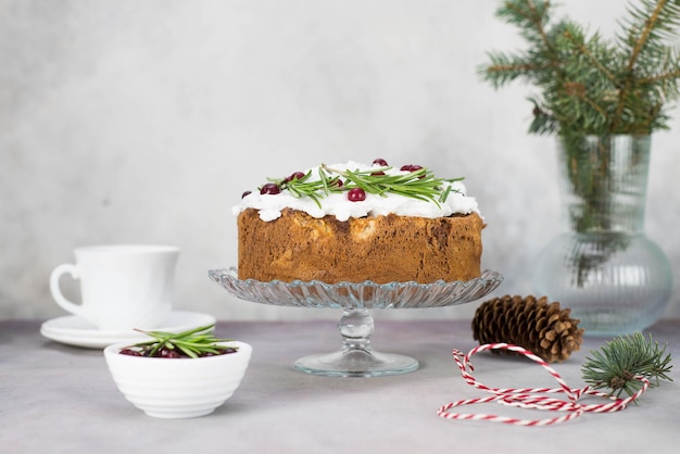 Weihnachtskuchen mit Rosmarin und roten Beeren auf einem Ständer auf grauem Hintergrund