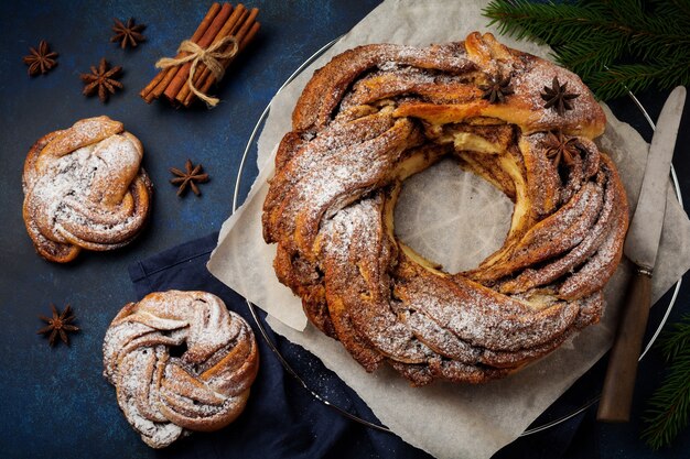 Weihnachtskuchenrolle mit Zimt und Puderzucker auf einem dunklen alten Beton- oder Steinhintergrund