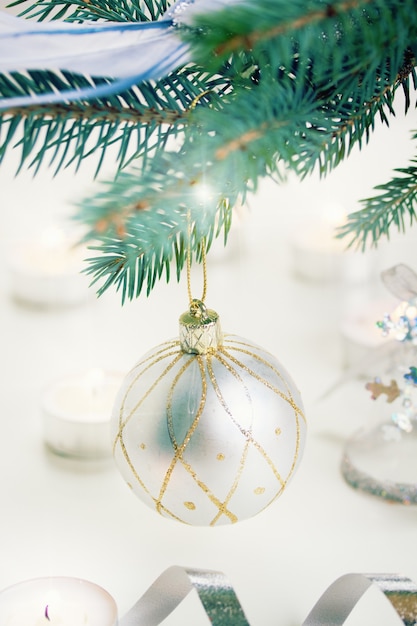 Weihnachtskugel hängt am blauen Tannenbaum und Kerzenlicht defokussiert Hintergrund