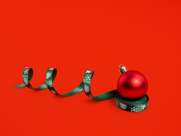 Weihnachtskugel-Serpentinenband auf rotem Hintergrund Neues Jahr das Konzept des Minimalismus