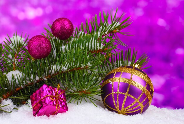 Weihnachtskugel und Spielzeug mit grünem Baum im Schnee auf Lila