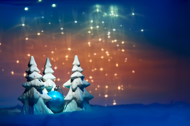 Weihnachtskugel zwischen Bäumen und Lichtern auf abstraktem Hintergrund