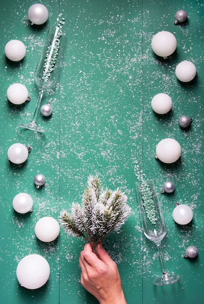 Weihnachtskugeln Champagnergläser Tannenzweige in der Hand auf einem grünen hölzernen Hintergrund mit Schnee