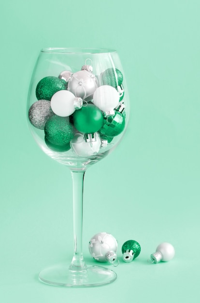 Weihnachtskugeln in einem Weinglas auf hellgrünem Hintergrund