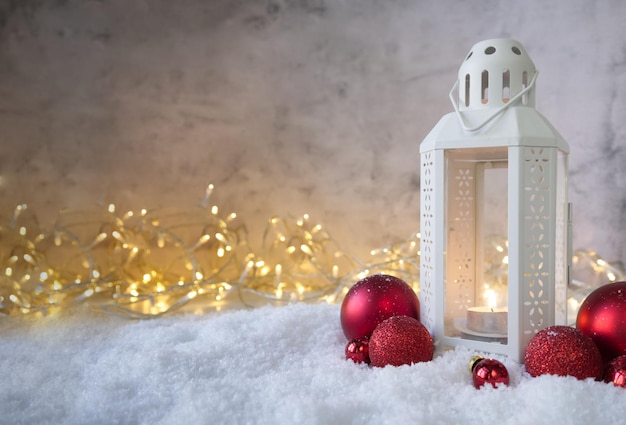 Weihnachtslaterne auf dem Schnee neben roten strukturierten Bällen vor dem Hintergrund von Lichtern