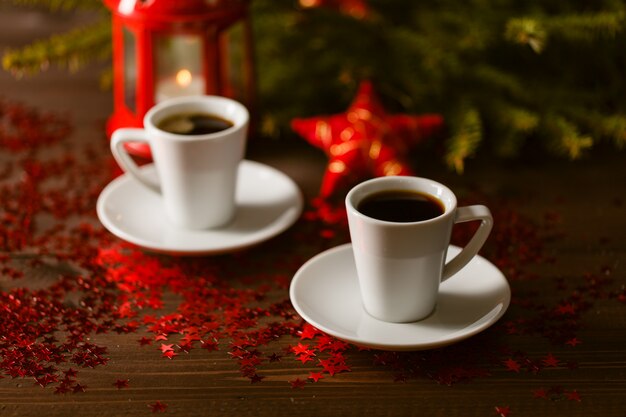 Weihnachtslaterne, die im Dunkeln mit silbernen Sternen auf rotem Tisch mit Kaffee glüht