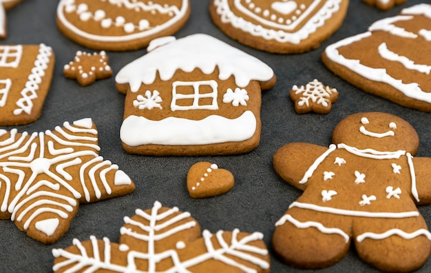 Weihnachtslebkuchen mit Zuckerguss auf grauem Hintergrund in Form eines Hauses und eines Lebkuchenmannes ein Weihnachtsbaum und Kugeln Sterne und Schneeflocken und Herzen Nahaufnahme