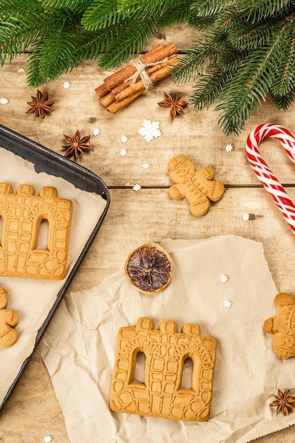 Weihnachtslebkuchenhaus und Lebkuchenmänner. Traditionelles festliches Neujahrsdesign, Kochprozess. Alter hölzerner Hintergrund, rustikaler Stil, Draufsicht