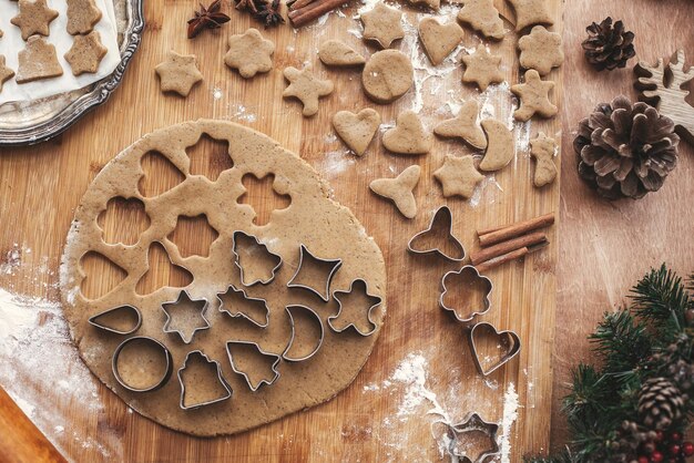 Weihnachtslebkuchenplätzchen flach legen Teig mit Metallschneidern auf rustikalem Tisch mit hölzernem Nudelholz Zimt-Anis-Kegel Weihnachtsschmuck Atmosphärisches stilvolles Bild