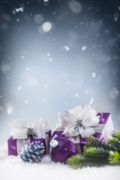 Weihnachtsluxuriöse lila Geschenke im Schnee und abstrakte schneebedeckte Atmosphäre.