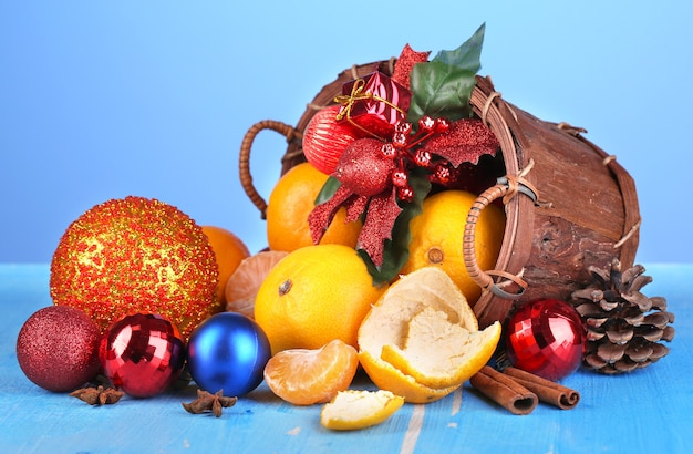 Weihnachtsmandarinen und Weihnachtsspielzeug im Korb auf Holztisch auf blauem Hintergrund