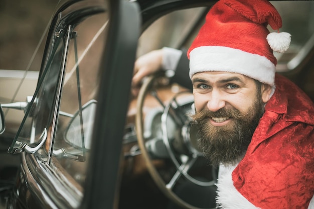 Weihnachtsmann-Fahrer, der am Rad im Retro-Autowinterferienfeier-Weihnachtsurlaub lächelt