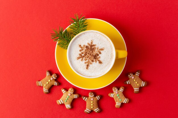 Weihnachtsmann geformter Lebkuchen um gelbe Tasse Kaffee auf rotem Hintergrund