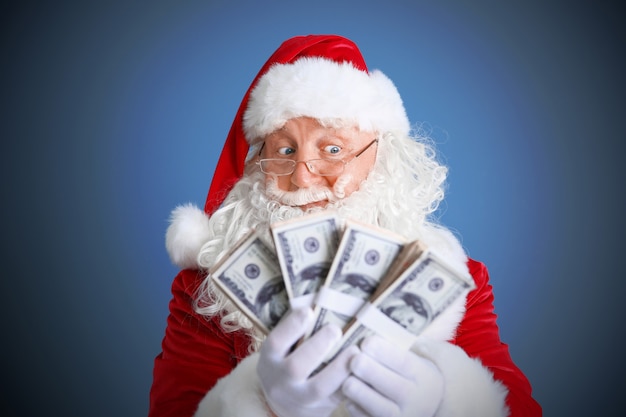 Weihnachtsmann hält Geld auf blauem Hintergrund