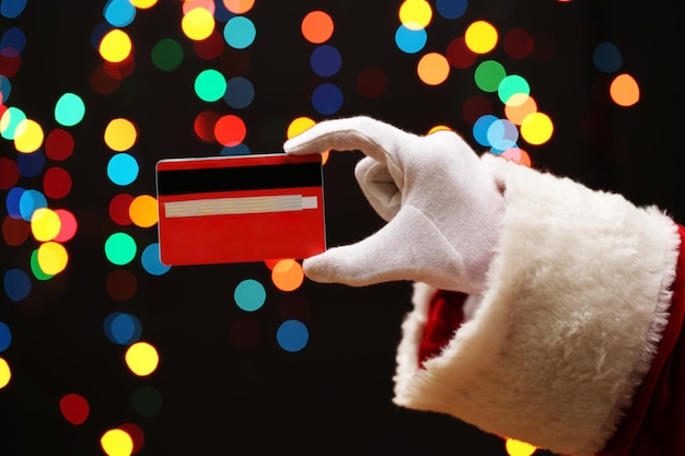 Weihnachtsmann-hand, die kreditkarte hält, auf girlandenhintergrund