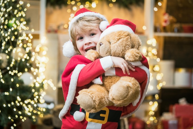 Weihnachtsmann-Helfer überraschten kleinen Weihnachtsmann-Junge in Umarmung Teddybär