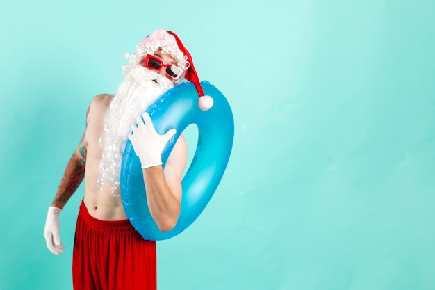 Weihnachtsmann in Anzug mit aufblasbarem Schwimmring in Sonnenbrille ruht am Strand