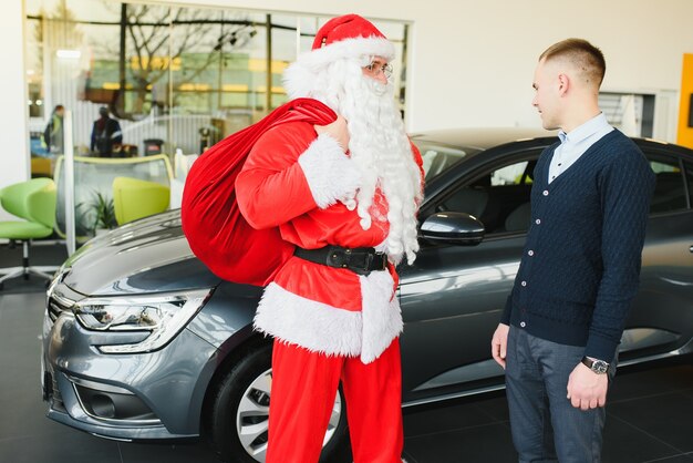 Weihnachtsmann in der Nähe eines Neuwagens in einem Autohaus.