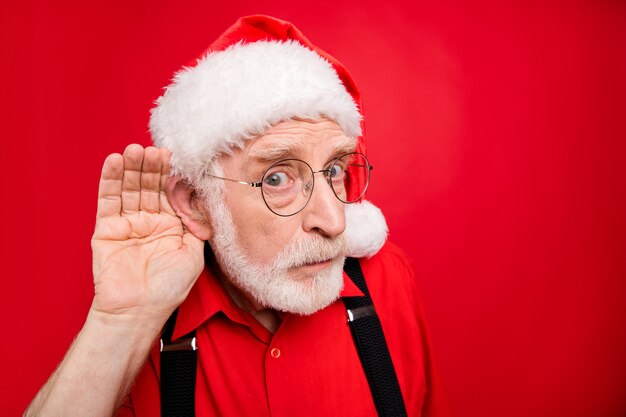 Weihnachtsmann in Hosenträgern und Hut posiert auf roter Wand